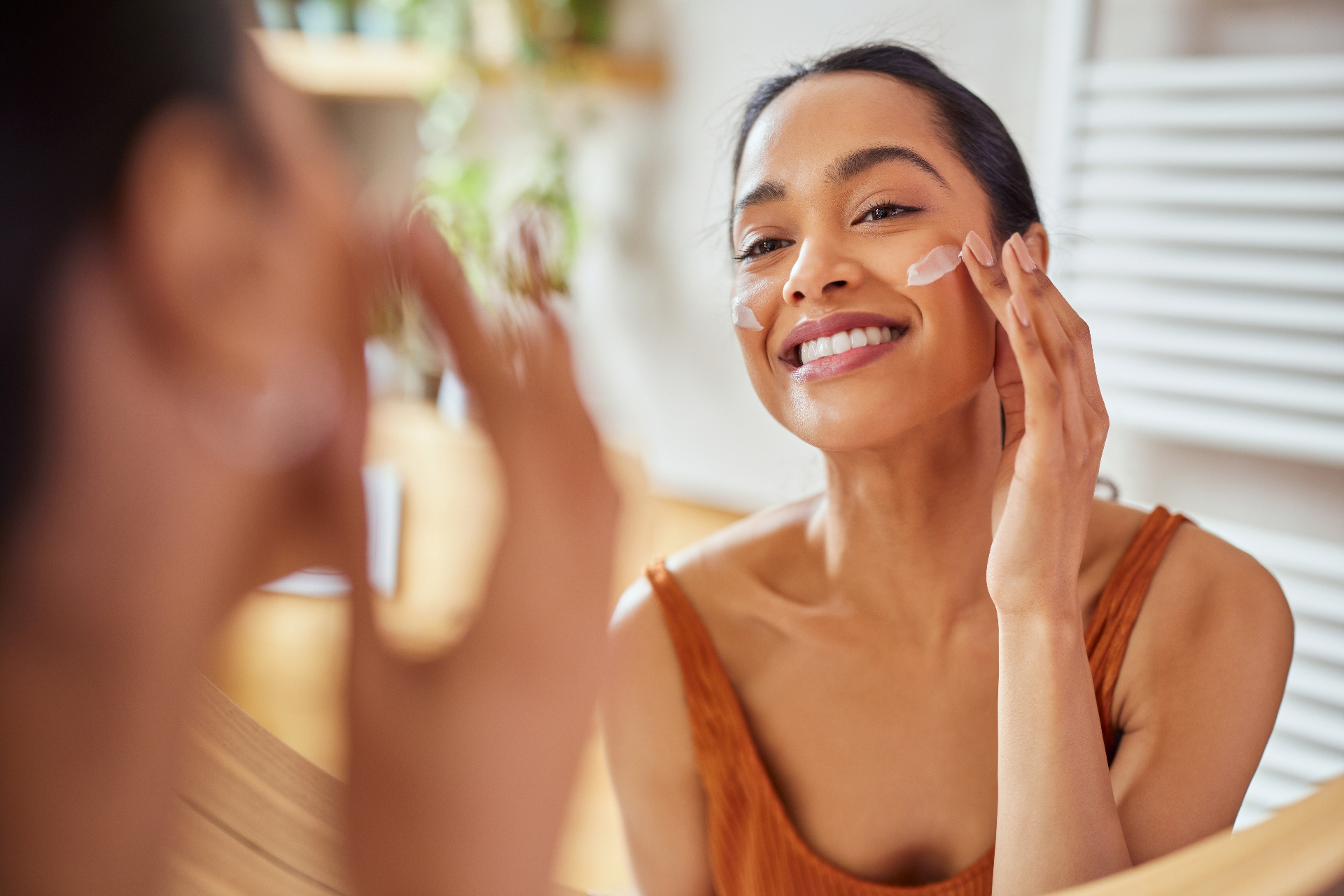 Person applying moisturiser in the bathroom mirror